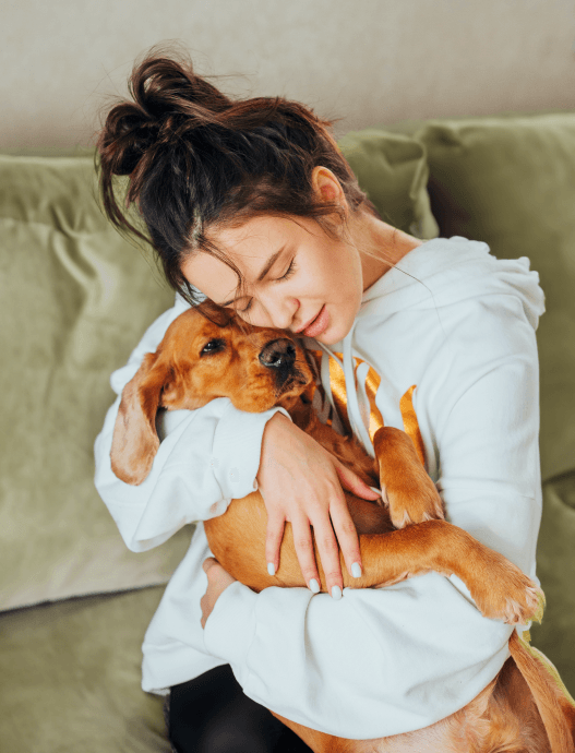 Lady lying on bed smiling with a brown dachshund puppy on her stomach with its tongue out